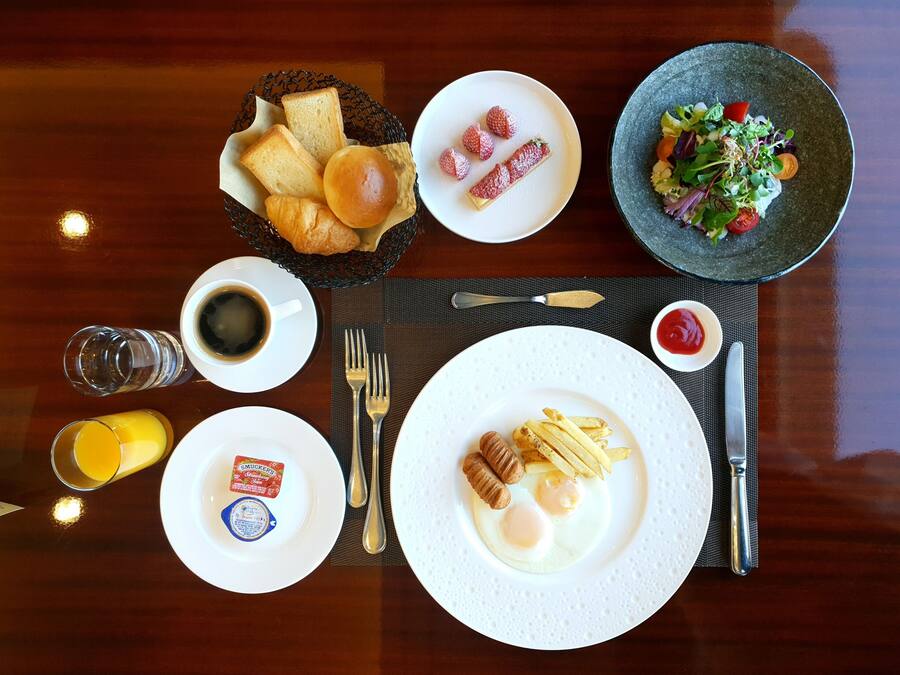 Colazione con pane tostato, croissant, fragole, insalata, uova, salsiccia e una bevanda.