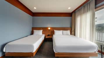Habitación de hotel con dos camas individuales, cabecera de madera, mesita de noche con teléfono y ventana con cortinas.