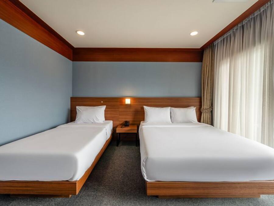 Habitación de hotel con dos camas individuales, cabecera de madera, mesita de noche con teléfono y ventana con cortinas.