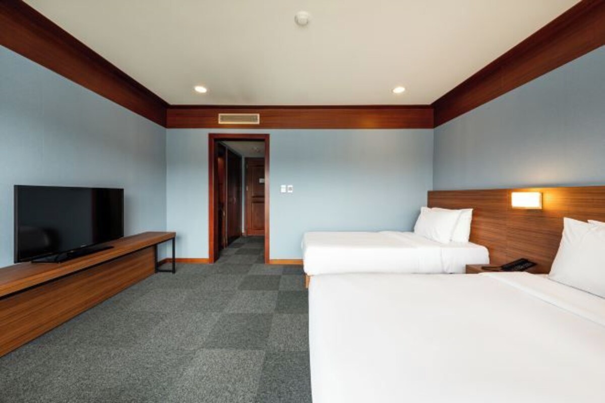 Een hotelkamer met een televisie, een bureau, twee bedden en een gang naar een andere kamer.