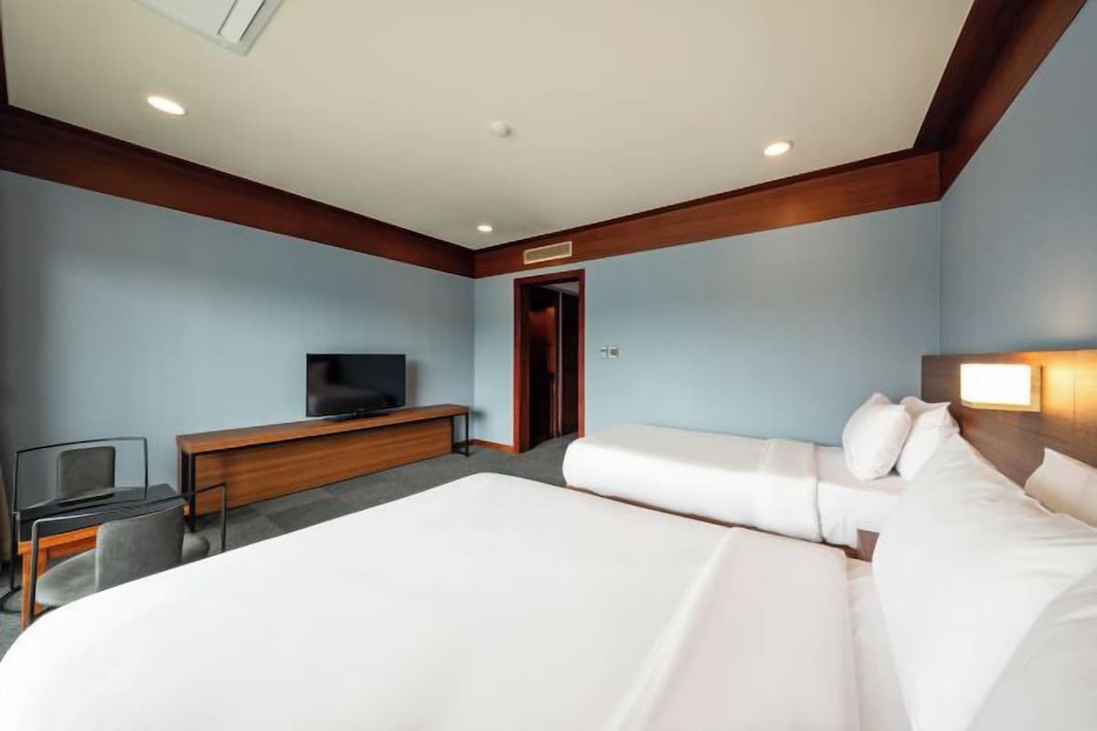 A hotel room with a bed, a desk, a television, and a door.