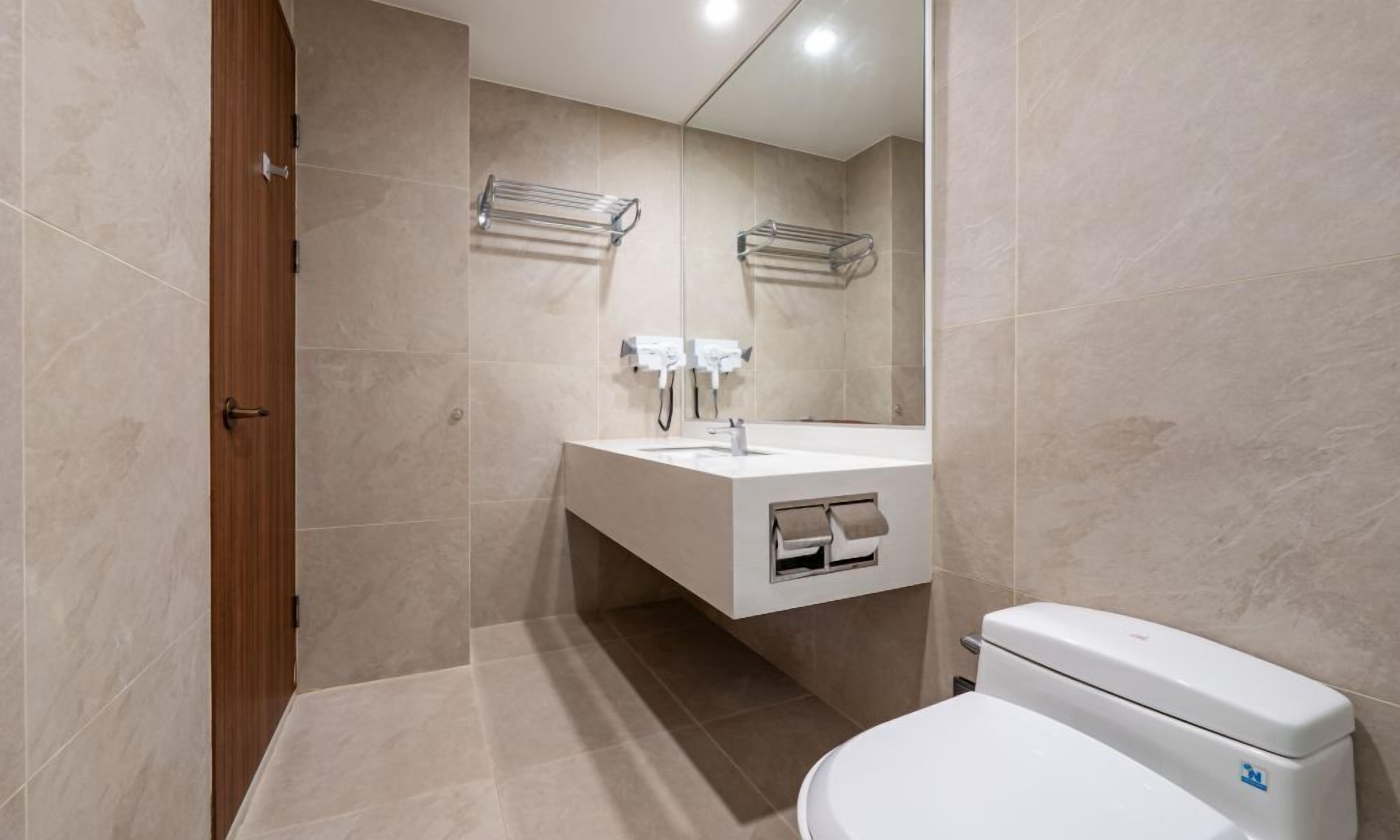 Une salle de bain moderne avec un lavabo blanc, un miroir et des toilettes. On y trouve des porte-serviettes au mur et une porte en bois.