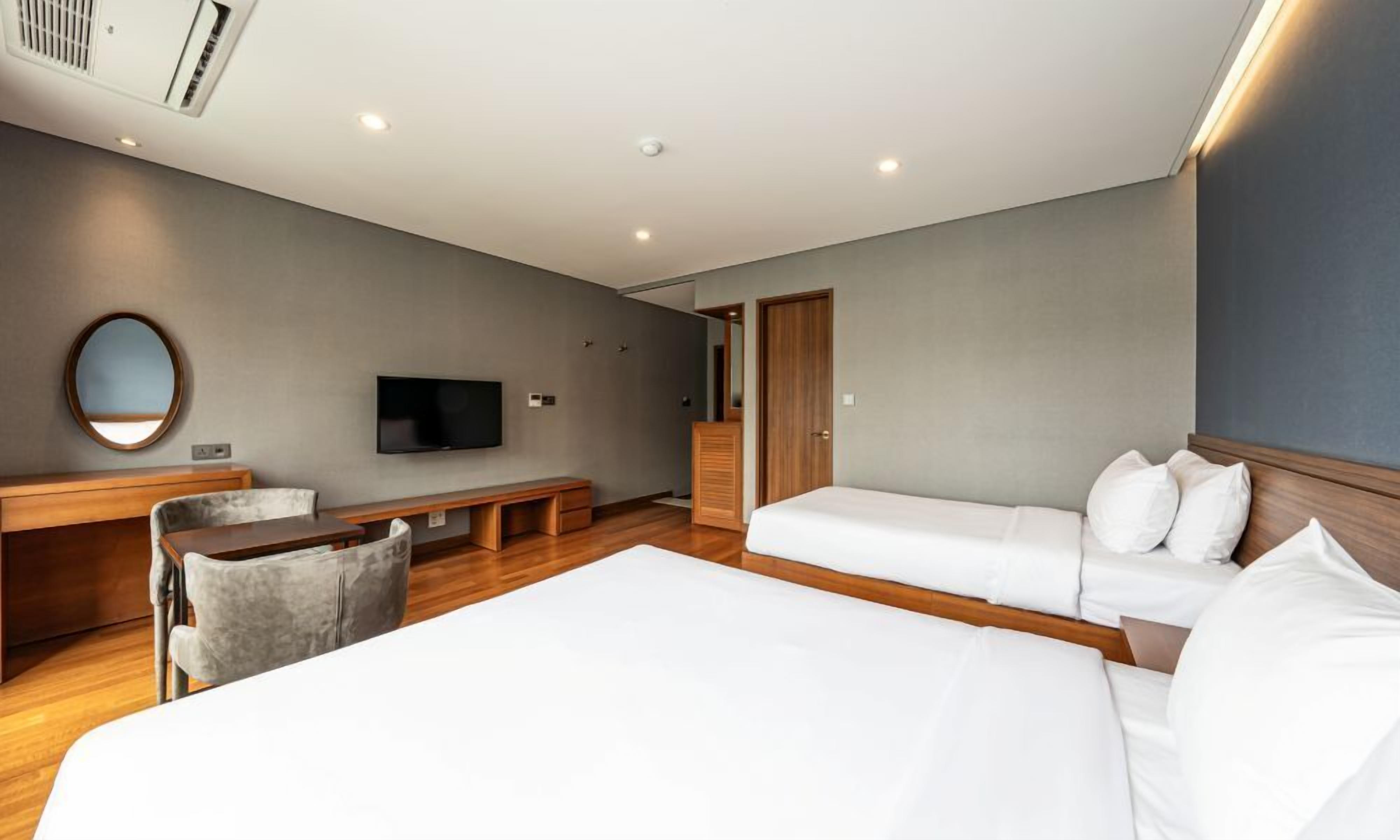 A hotel room with a large bed, a smaller bed, a desk with a chair, a TV, and a mirror on the wall.