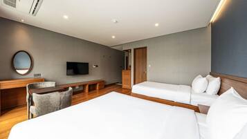 Habitación de hotel con una cama grande, otra más pequeña, un escritorio con silla, televisor y un espejo en la pared.