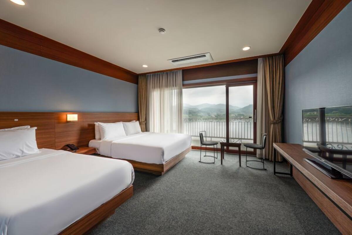 A hotel room with two beds, a TV, a balcony with a view, and a desk with a chair.