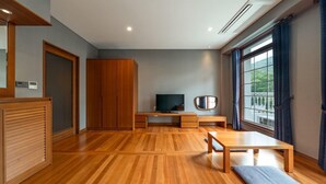 Una habitació moderna amb un terra de fusta, una televisió, una banca i una finestra amb cortines.