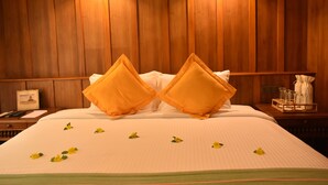 Ein Hotelzimmer mit einer Holzwand, einem ordentlich bezogenen Bett mit zwei Kissen sowie einem Nachttisch mit einem Tablett mit Gläsern und einer Taschentuchbox.