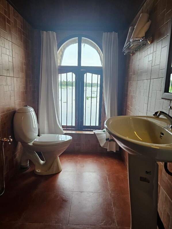 A bathroom with a toilet, sink, and a window with curtains. - Kumarakom Lake Resort Houseboats (Kumarakom)