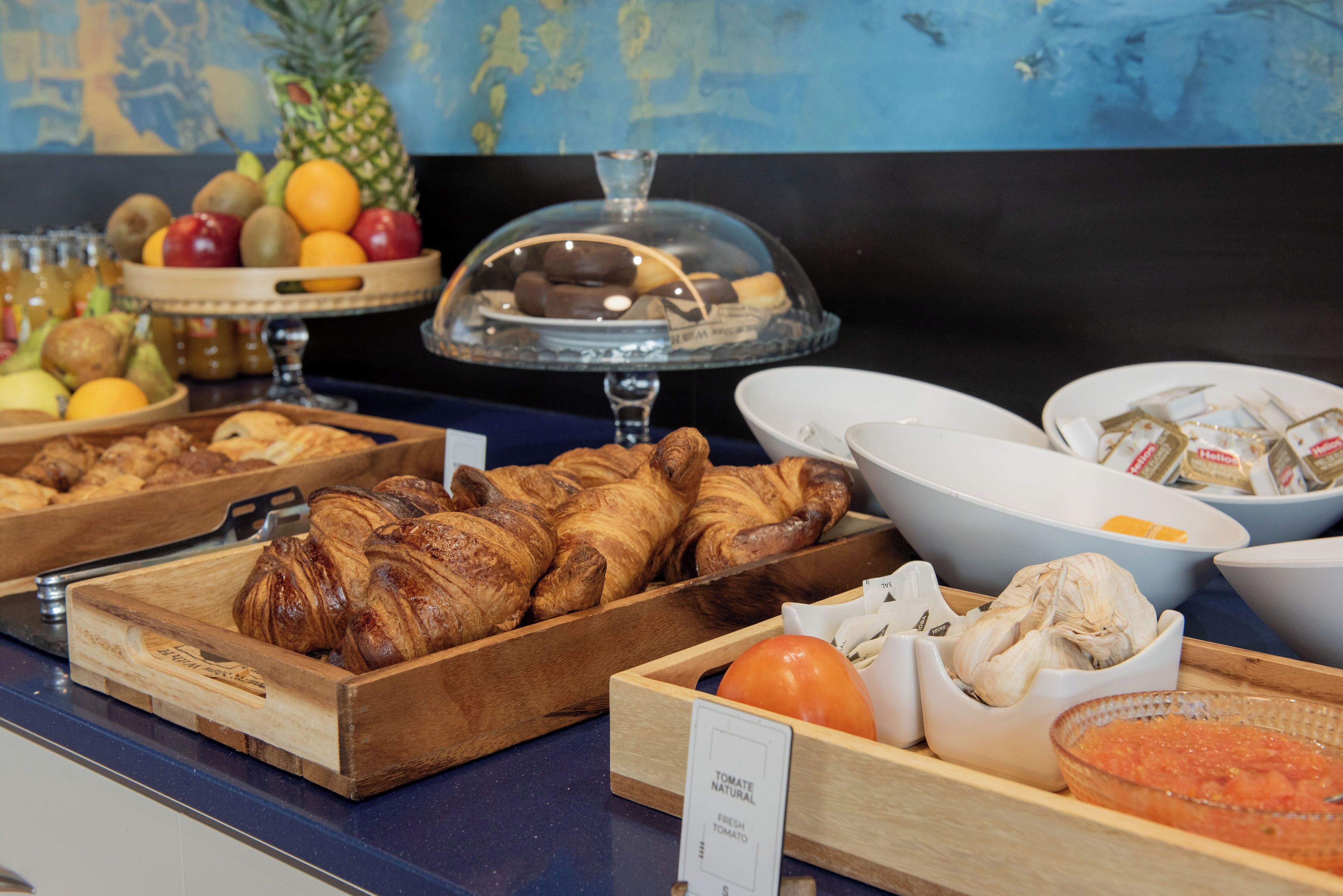 A buffet with various food items including croissants, fruits, and condiments.
