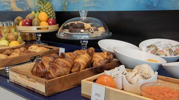 A buffet with various food items including croissants, fruits, and condiments.