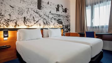 Habitación de hotel con dos camas, un mural abstracto grande en la pared, un escritorio con silla y una ventana con cortinas.