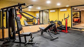 Une salle de sport équipée de divers appareils d’exercice, avec un miroir et un mur jaune.