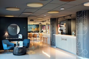 Un vestíbulo moderno de hotel con una recepción, zona de estar y vistas a la cocina.