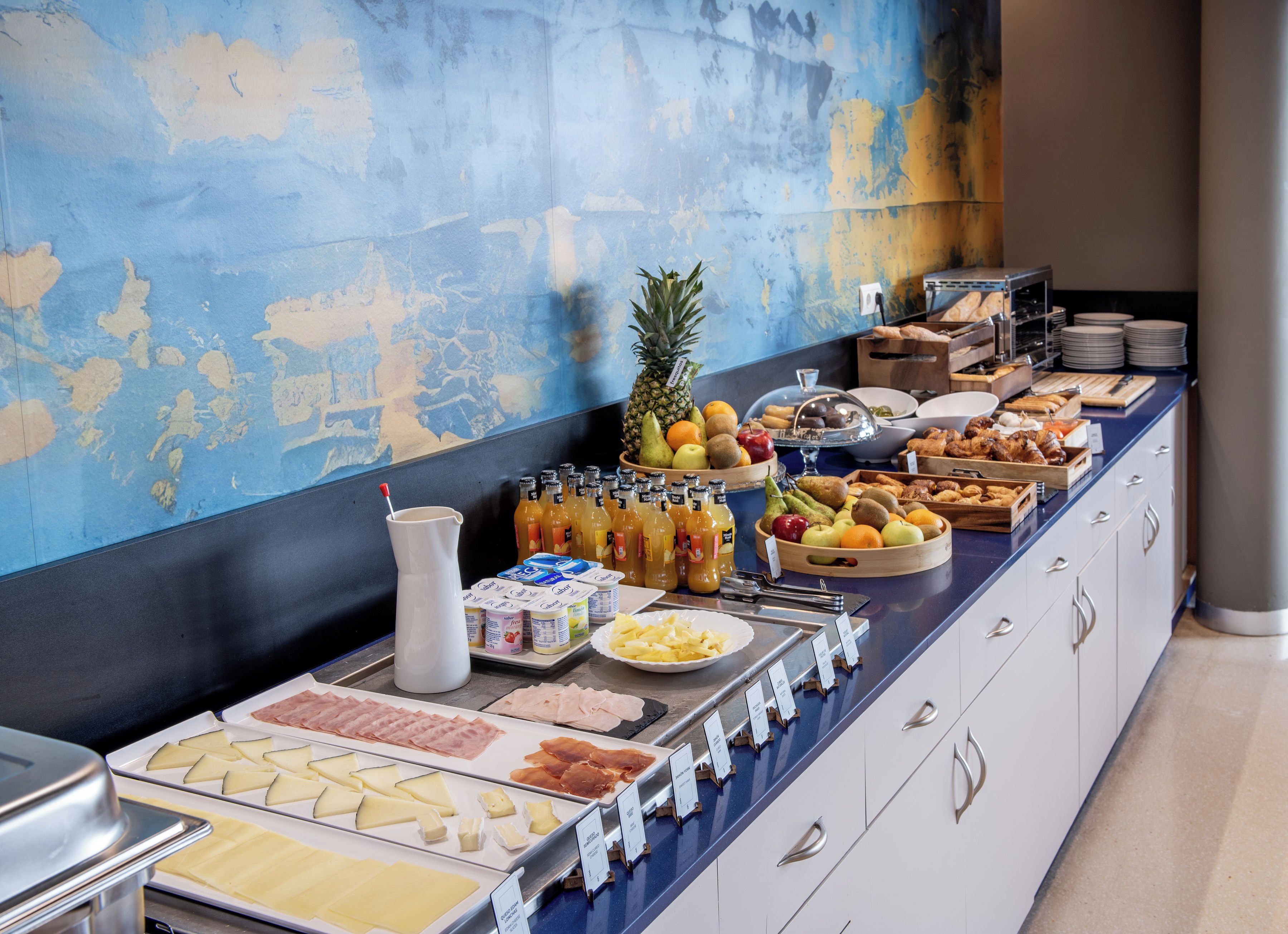 Een buffet met diverse gerechten, waaronder fruit, kazen en vleeswaren, gepresenteerd op een toonbank met een blauw-witte kleurstelling.