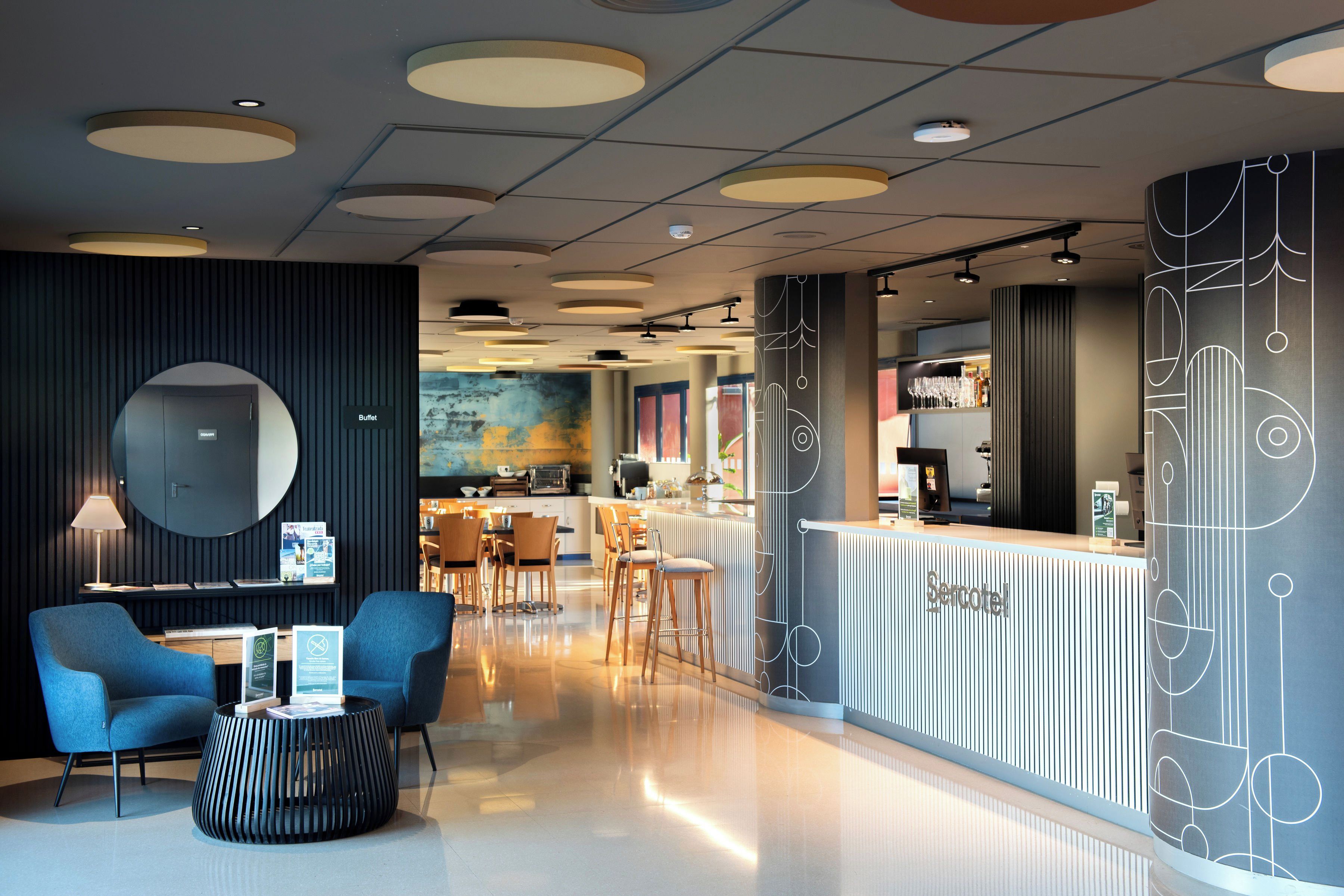Een moderne hotellobby met een receptiebalie, een zithoek en een bar.