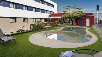 A modern hotel courtyard with a swimming pool, lounge chairs, and a well-maintained lawn.