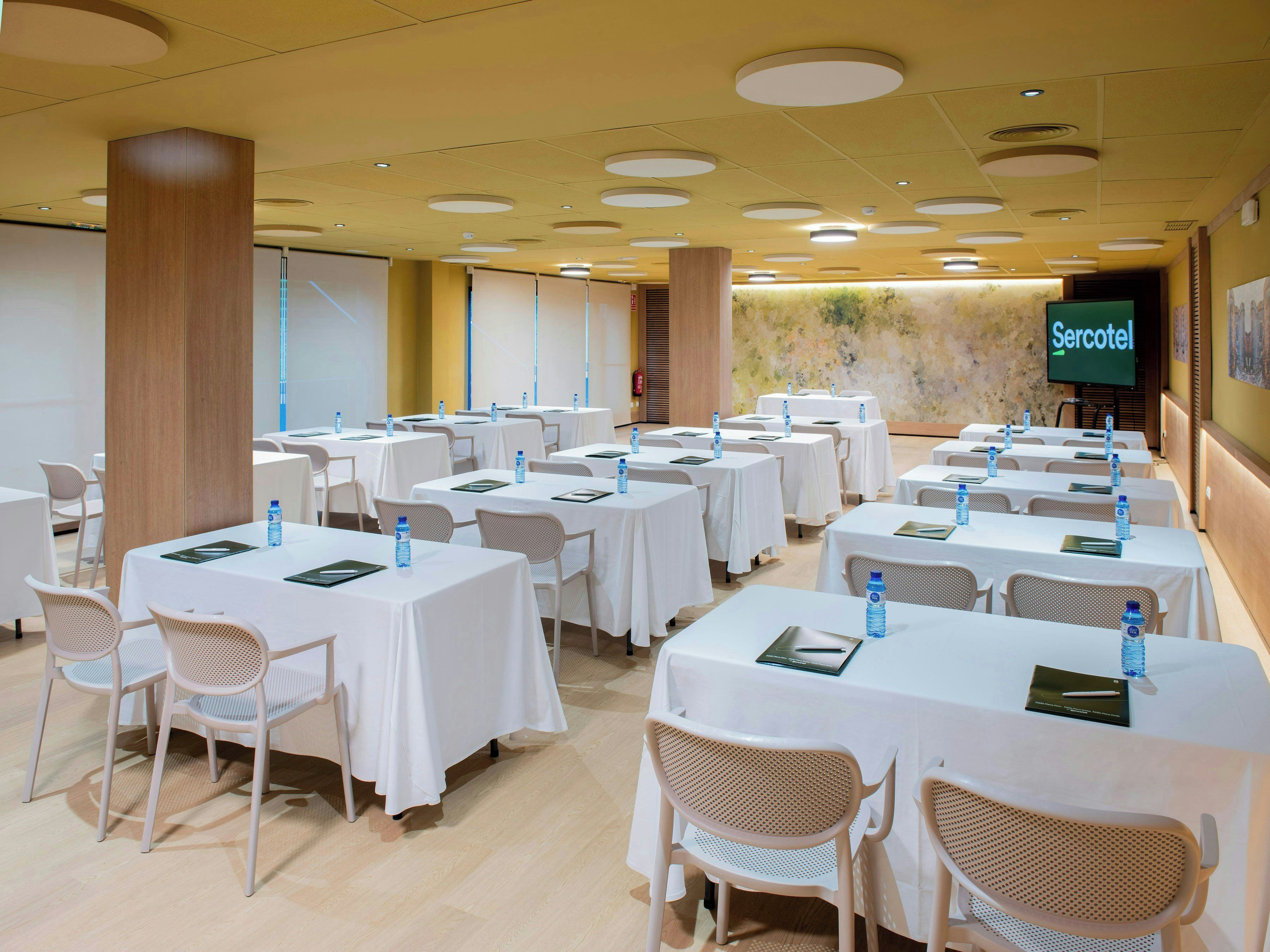Une salle de conférence équipée de plusieurs tables et chaises, de bouteilles d’eau et d’un écran affichant le logo « Sercotel ».