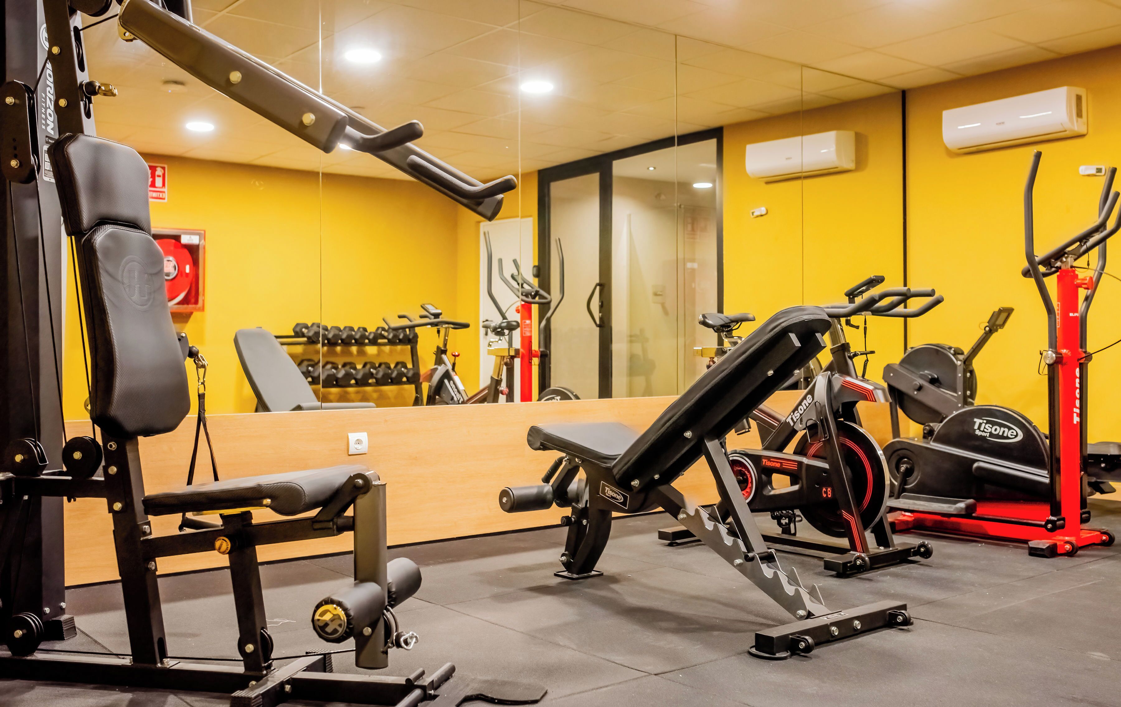Un gimnasio con varios equipos de ejercicio, incluyendo una prensa de banca, mancuernas y máquinas de cardio.
