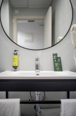 A bathroom with a white sink, a mirror, a hairdryer, and toiletries. - Hotel Sercotel Plana Onda (Onda)