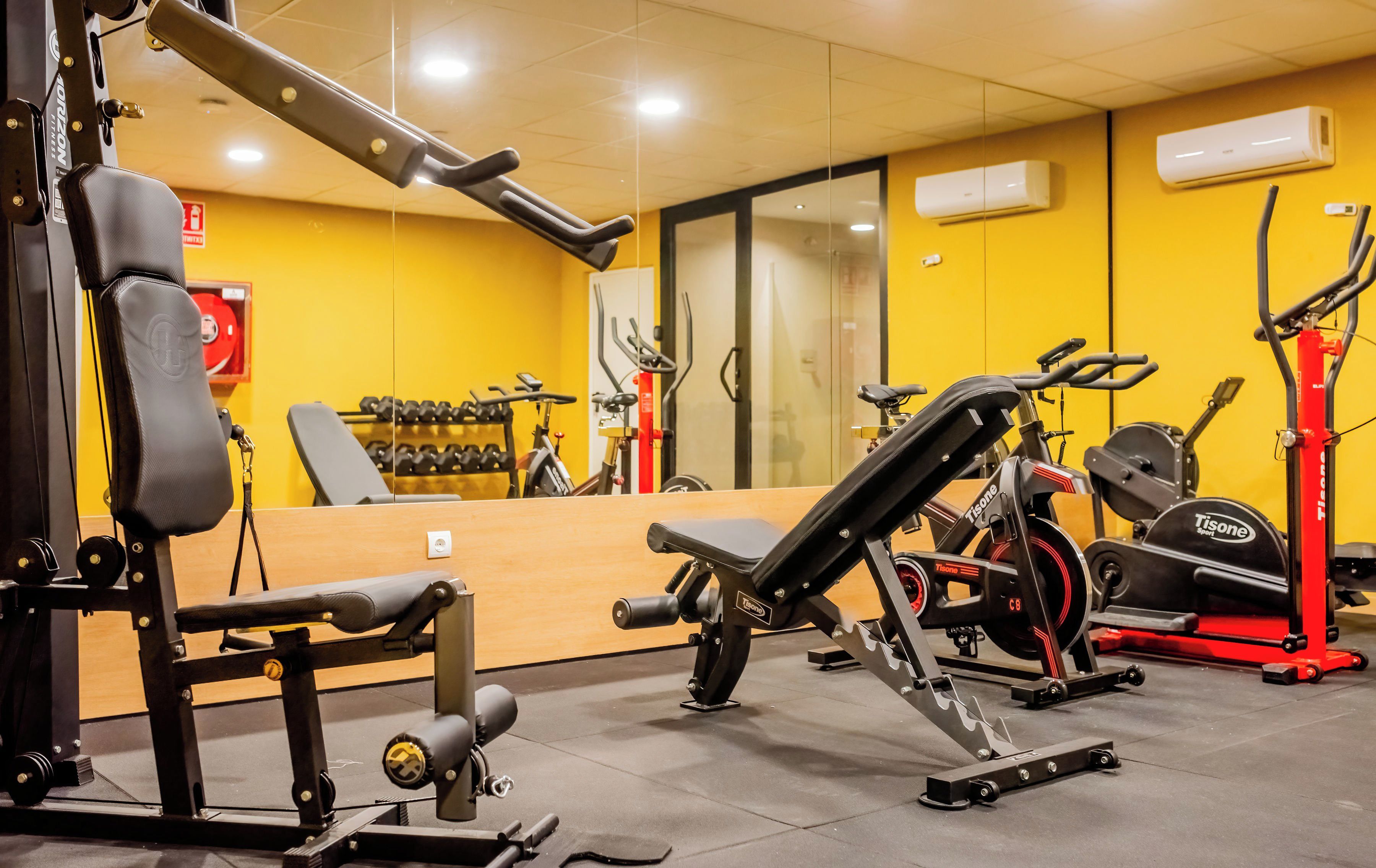 Un gimnasio con diverso equipo de ejercicio, incluyendo una prensa de banca, mancuernas y una bicicleta estática.