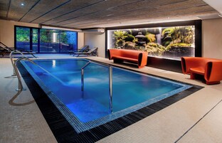 Una piscina interior moderna con agua cristalina, una zona de estar con sillones naranjas y un gran acuario.