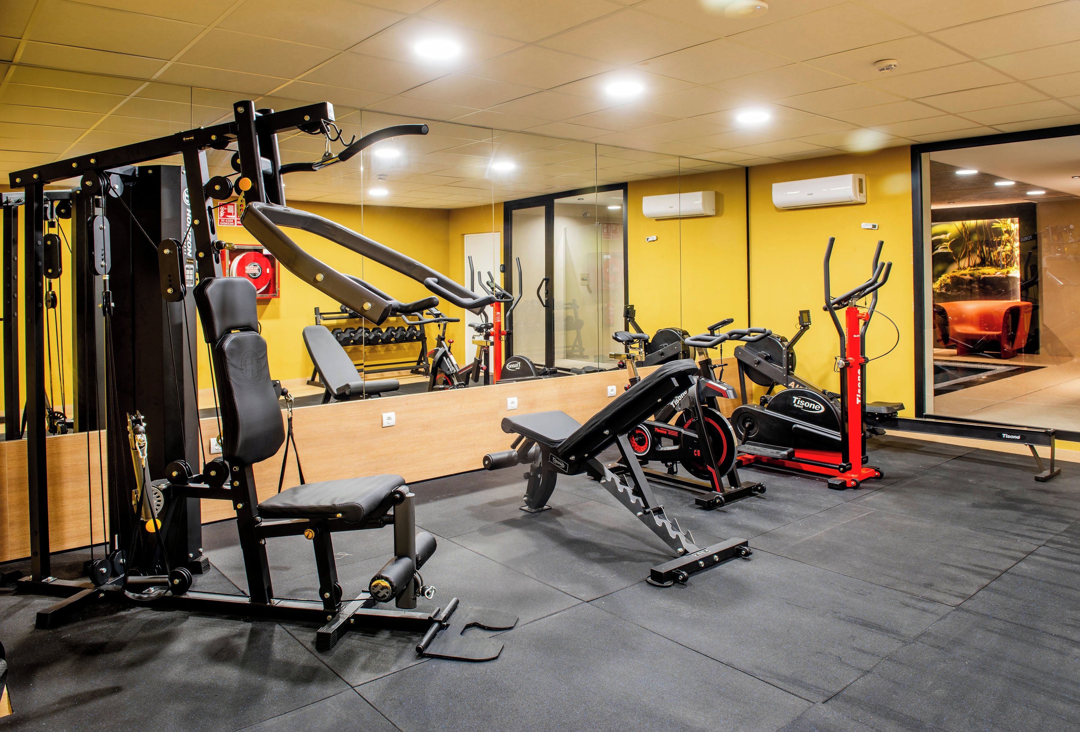 Un gimnasio con diferentes equipos de ejercicio, un espejo y una pared amarilla.