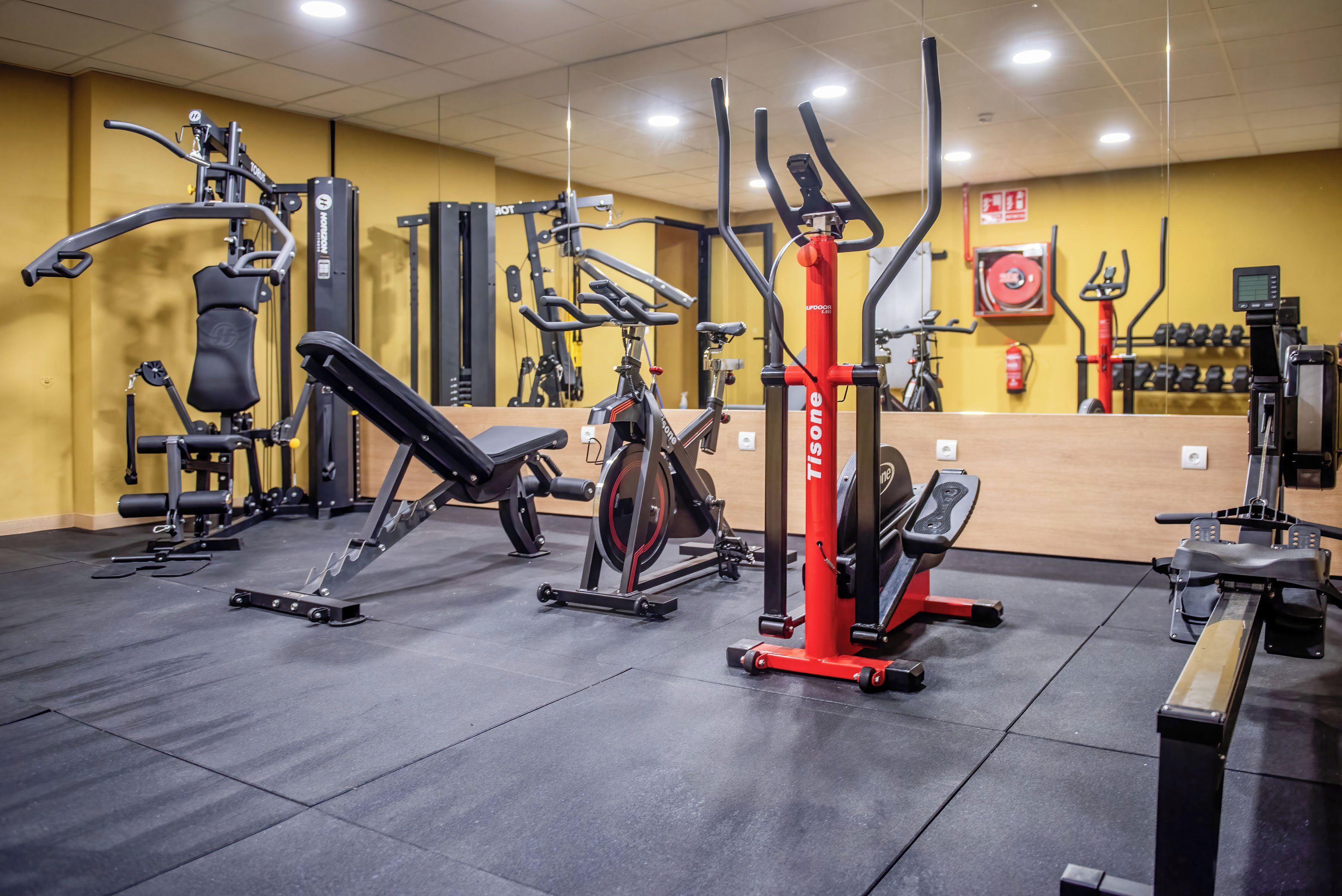 Un gimnasio con diversos equipos de ejercicio, incluyendo una máquina de remo, una prensa de piernas y una bicicleta estática.