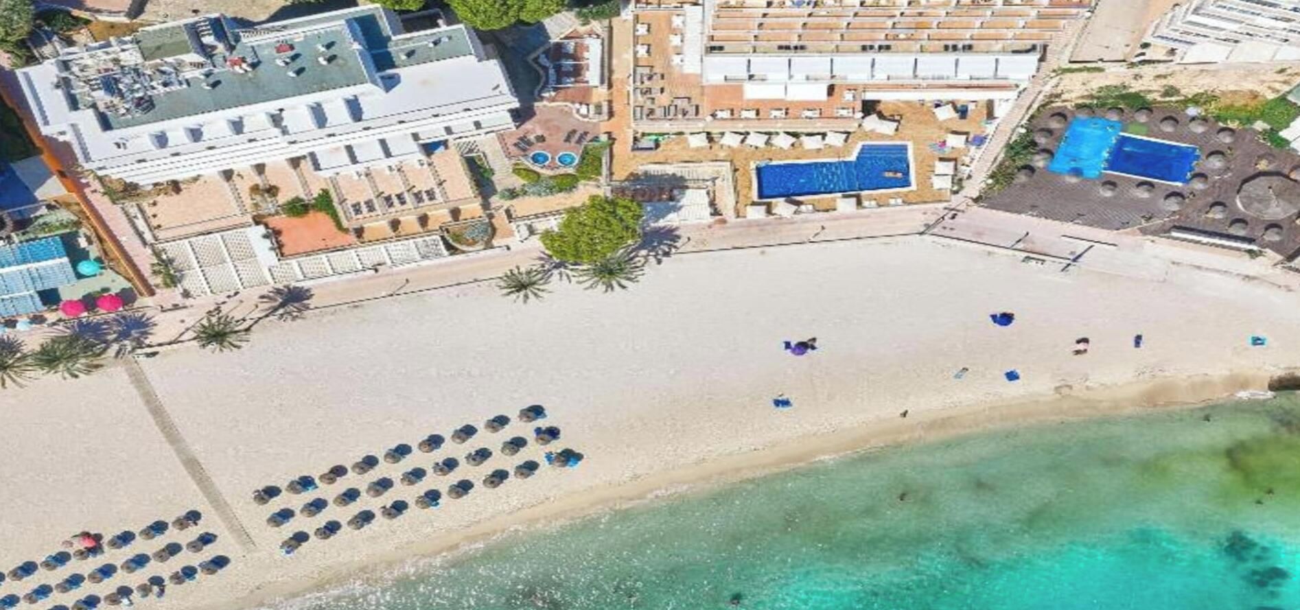 An aerial view of a beachside hotel with a pool, beach umbrellas, and a clear view of the ocean.