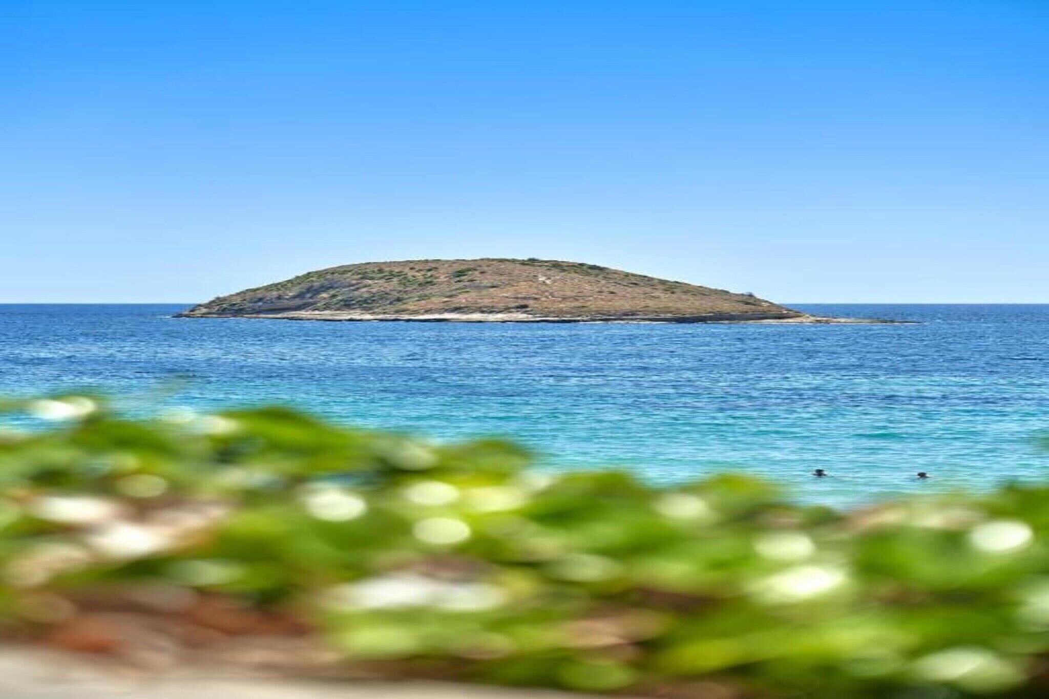 A small island with clear blue waters and a distant view of the sky.