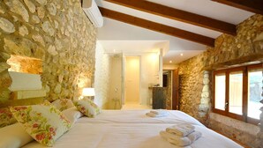 Um quarto com paredes de pedra, teto de madeira, cama com almofadas florais e janela com vista.