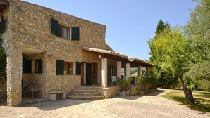 A stone building with a covered porch, outdoor seating, and a paved entrance. - Villa in Majorca near Tramuntana Mountains (Manacor de la Vall)