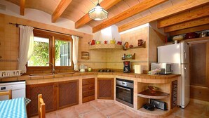 A compact kitchen with wooden cabinets, a built-in oven, a refrigerator, and a window with curtains. - Villa in Majorca near Tramuntana Mountains (Manacor de la Vall)