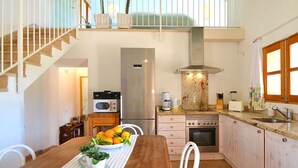 Cocina compacta con refrigerador, microondas, estufa y pileta. Hay una mesa de comedor con frutero y sillas. Una escalera conduce a un nivel superior.