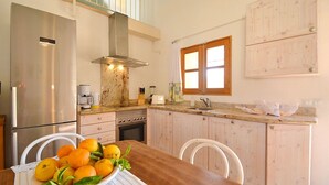 Una cocina con un refrigerador de acero inoxidable, una estufa y un lavabo. Hay una mesa de comedor de madera con un tazón de naranjas y limones.