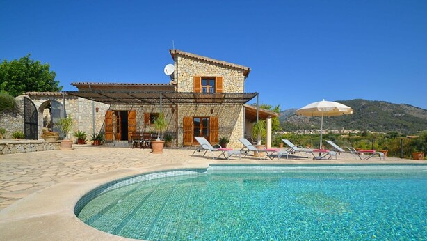 Una villa de piedra con piscina, sillas de descanso y montañas al fondo.
