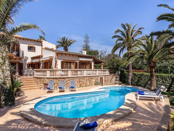 A poolside area with a curved pool, lounge chairs, and a stone wall.
