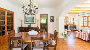 Un comedor con una mesa de madera, sillas, una araña y un cuadro en la pared.