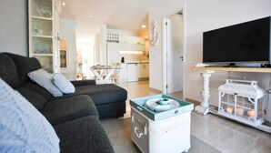 Una sala moderna con sofá, mesa de centro, televisor y cocina al fondo.