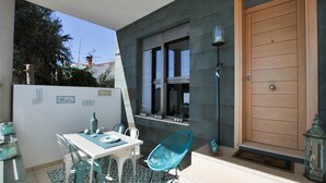 Un patio con mesa y sillas, una puerta de madera y una ventana con plantas en macetas.