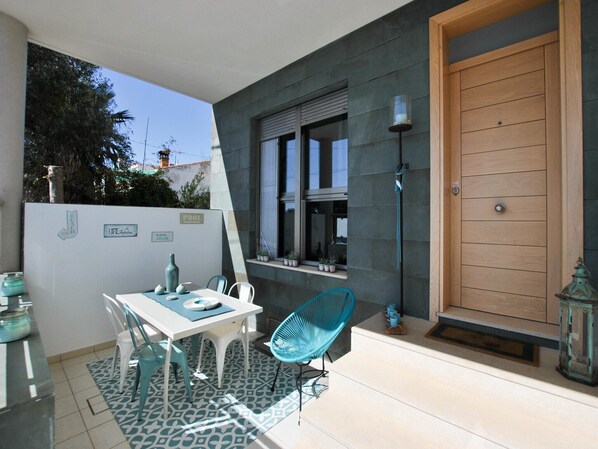 A patio area with a table and chairs, a wooden door, and a window with potted plants.