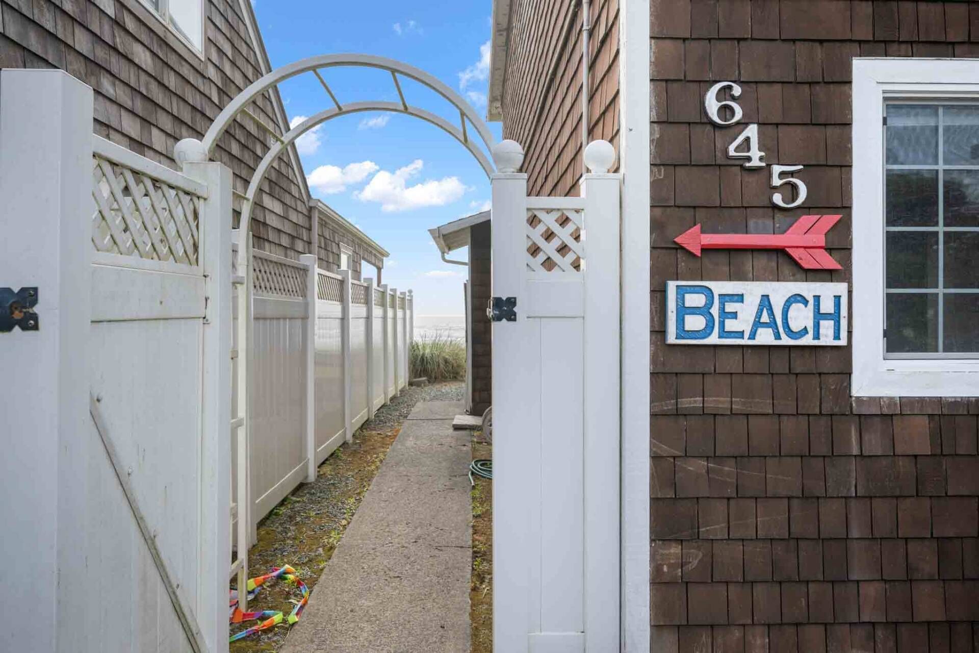 Un étroit sentier mène à une entrée fermée par un portail, sur laquelle on peut lire l’inscription « Plage », et une flèche indique la direction à suivre, vers la gauche.