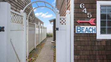Un étroit sentier mène à une entrée fermée par un portail, sur laquelle on peut lire l’inscription « Plage », et une flèche indique la direction à suivre, vers la gauche.