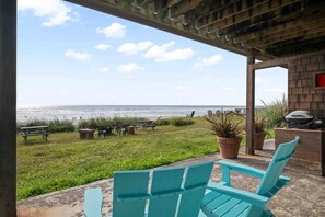 Un patio exterior con vista al océano, con varias sillas, una mesa y una parrilla de barbacoa.