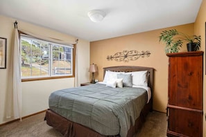 Un dormitorio con cama, mesita de noche, lámpara, ventana con cortinas, un elemento decorativo en la pared y un armario.
