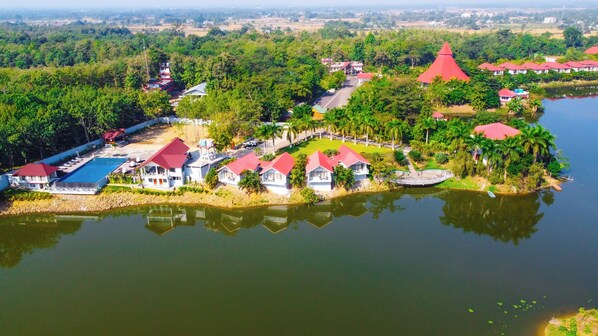 Un complejo turístico junto al lago con varios edificios de techo rojo, una piscina y un muelle.