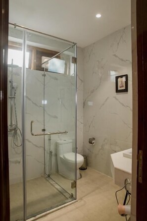 Bathroom features a glass-enclosed shower with handheld showerhead and glass door, a toilet with white porcelain design, and a framed picture on the wall.