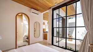Een moderne slaapkamer met een groot bed, een inloopkast, een badkamer en uitzicht op het groen door grote ramen.