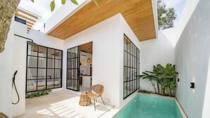 Een modern buitenzwembad met een houten plafond, grote ramen en een zitgedeelte met rieten stoelen.