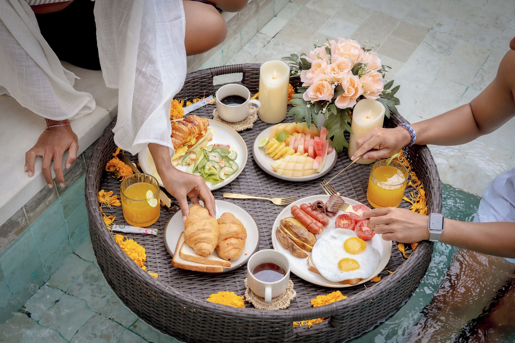 Une table en osier, dressée pour le petit-déjeuner, avec des croissants, des œufs, des saucisses et des fruits.