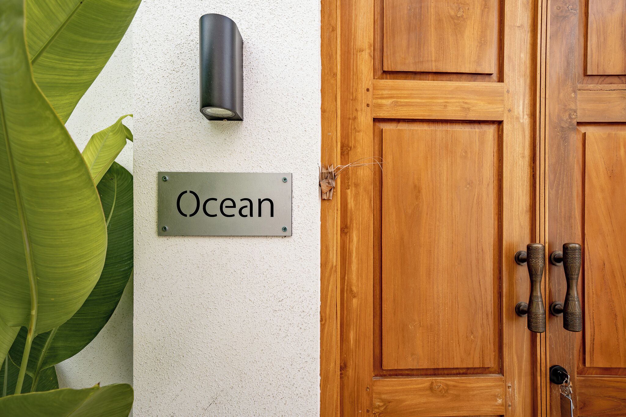 Una puerta de madera con un picaporte metálico, un letrero que dice "Ocean" y una lámpara de pared.